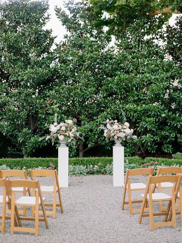 two tall white vases with flowers on each stand in the middle of an outdoor ceremony