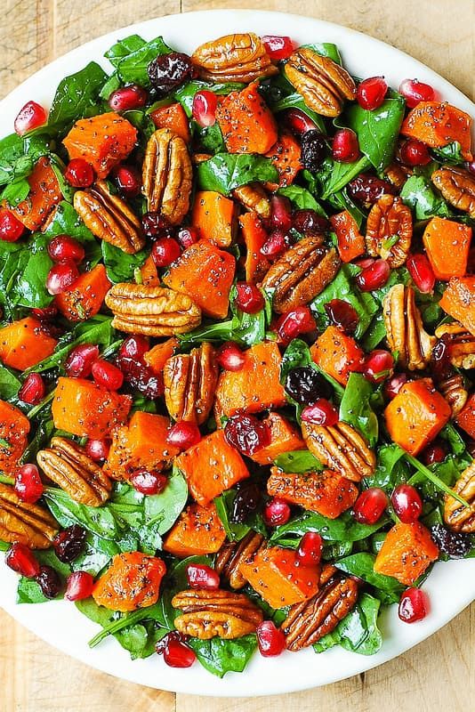 a white bowl filled with salad topped with nuts and cranberries on top of a wooden table