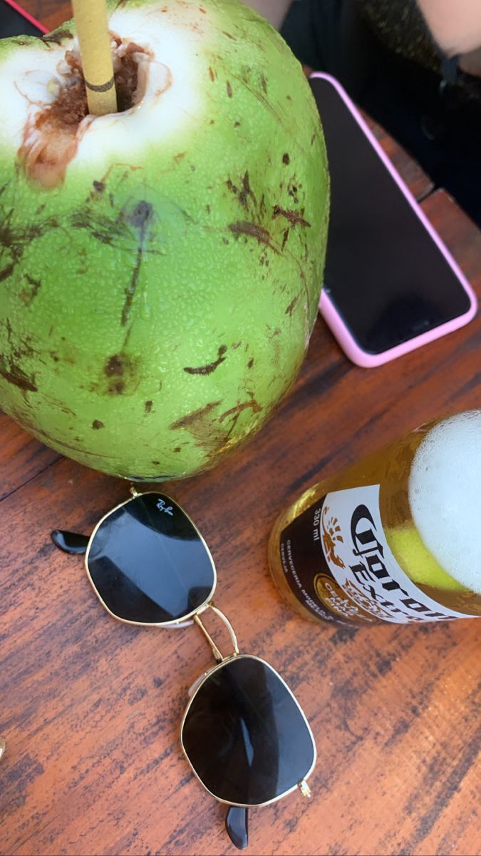 a green apple sitting on top of a wooden table next to sunglasses and a drink