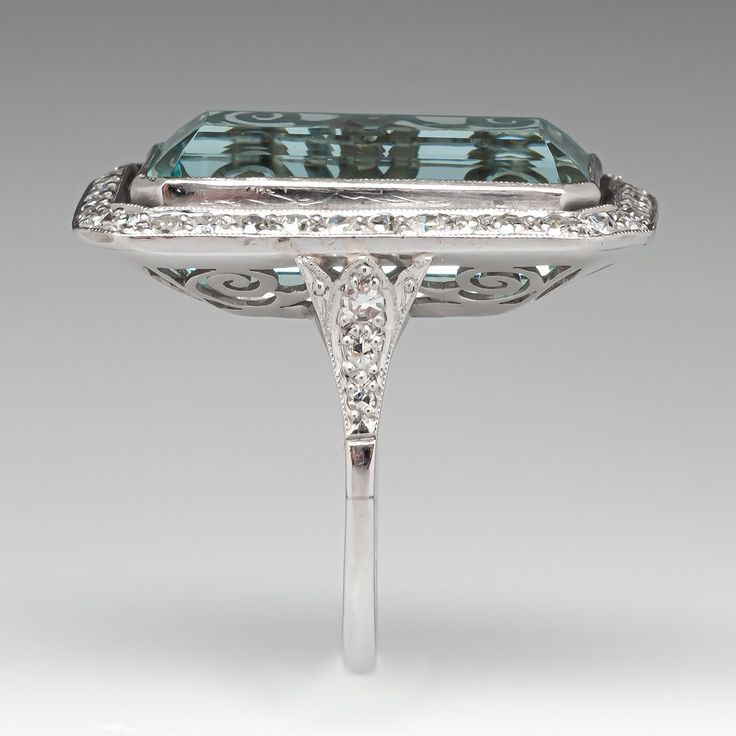 This mazing vintage cocktail ring is centered with one (1), bezel set, emerald cut natural aquamarine that is bordered with thirty-six (36), bead set, round single cut diamonds. The shoulders of the ring are each accented with three (3), bead set, round single cut diamonds. The gemstones are bordered with milgrain edging. The ring measures 28.9mm X 18.7mm at the top, rises 9.1mm above the finger, tapering to 1.7mm wide and 1.3mm thick at the base of the shank. It is currently a size 7. Formal Emerald Ring With Diamond And Rectangular Stone, Elegant Octagonal Topaz Ring, Formal Emerald Ring With Rectangular Diamond, Art Deco Baguette Cut Stone Jewelry, Elegant Octagon Emerald Ring In Platinum, Formal White Gold Topaz Ring With Rectangular Stone, Elegant Emerald Cut Topaz Ring With 17 Jewels, Elegant Emerald Cut Topaz Ring, Collectible Art Deco Emerald Ring