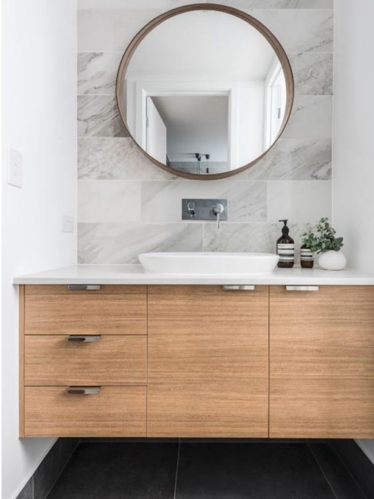 a bathroom with a round mirror above the sink and wooden cabinetry on the side