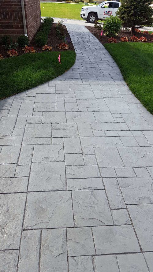 a brick walkway leading to a car parked on the side of a road in front of a house