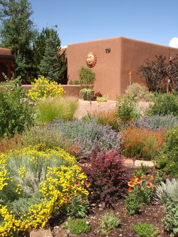 an adobe - style house surrounded by colorful flowers and trees in front of the building