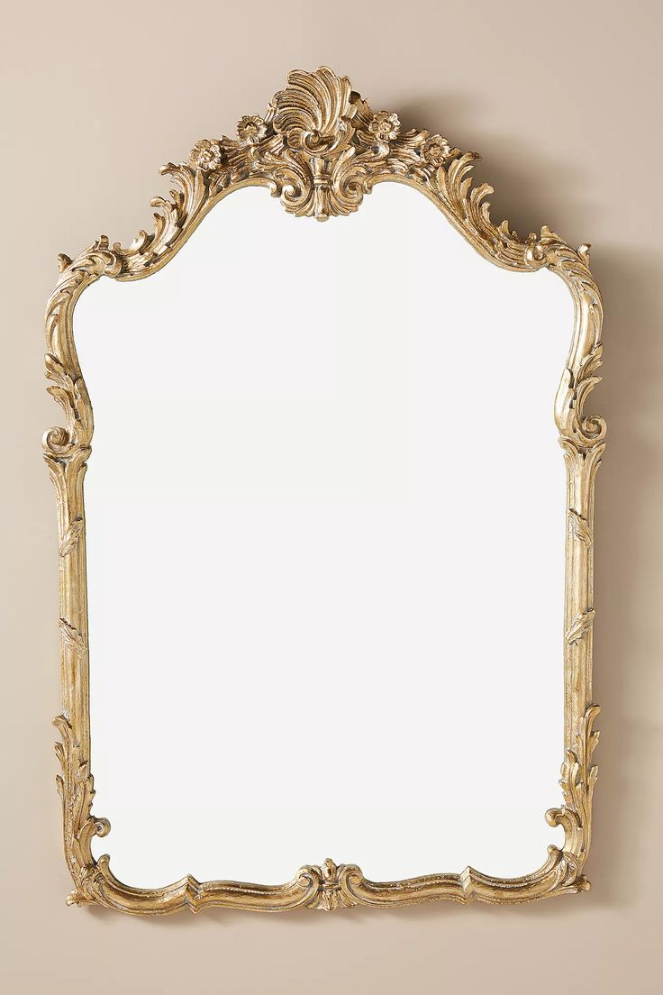 an ornate gold framed mirror hanging on the side of a wall with a white background