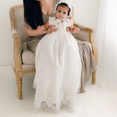 a woman is holding a baby in a white dress while she sits on a chair