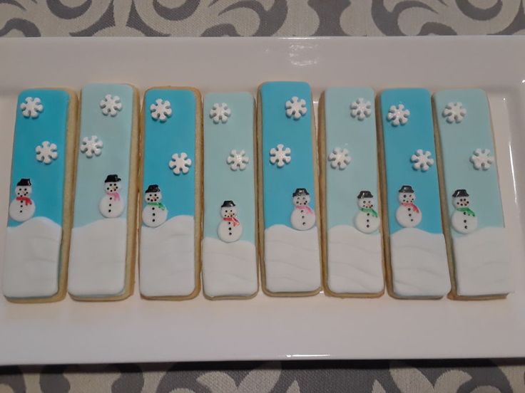 decorated cookies in the shape of snowmen on a white platter with blue background