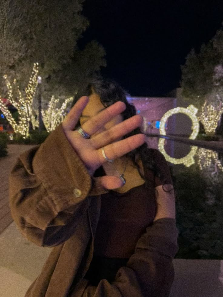 a woman sitting on the ground with her hand up to her face while holding a cell phone