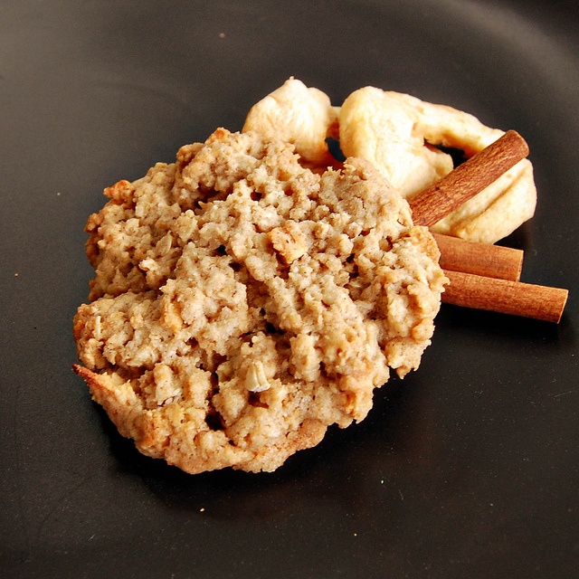 an oatmeal cookie and cinnamon sticks on a black plate