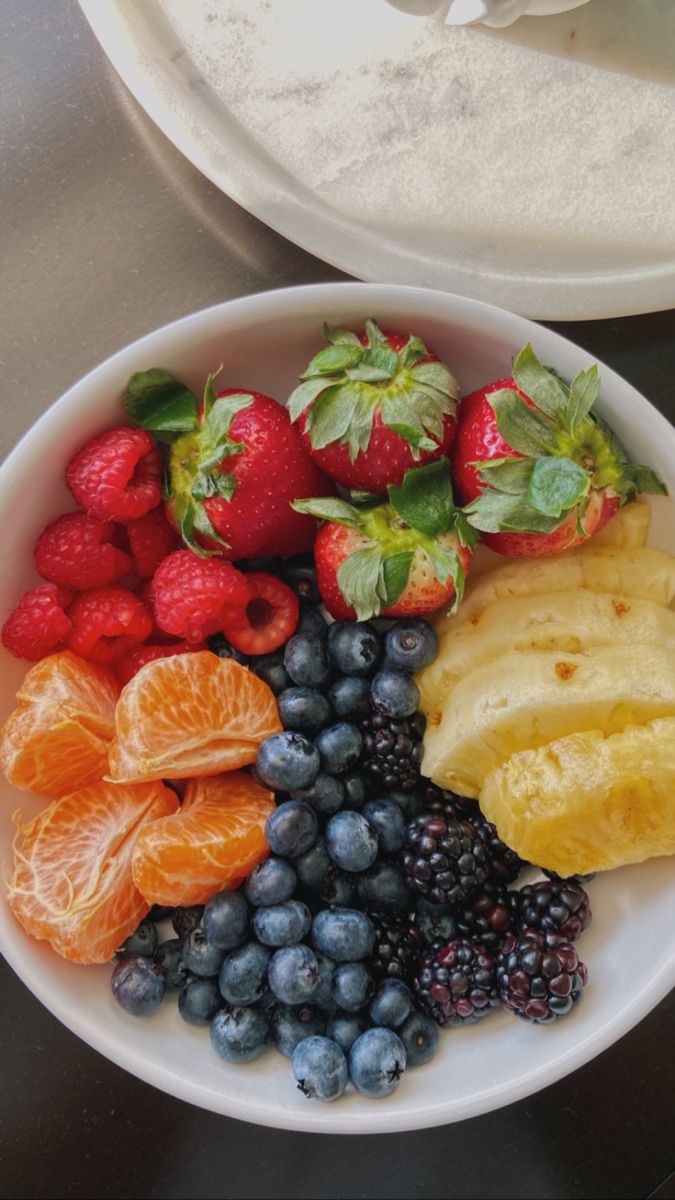 a white bowl filled with fruit on top of a metal counter next to a plate