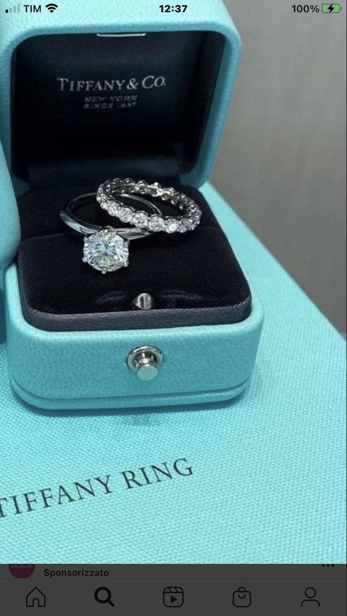 two wedding rings in a blue box on top of a white table with the words tiffany ring