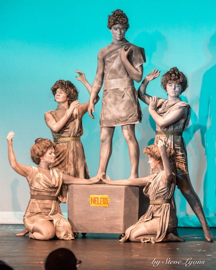 five people standing on top of a wooden box in front of a blue wall and statue