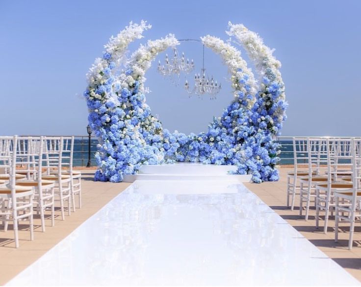 an outdoor ceremony setup with blue and white flowers on the aisle, chandelier and chairs