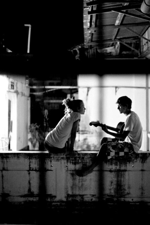 black and white photograph of two people sitting on the edge of a building playing guitar