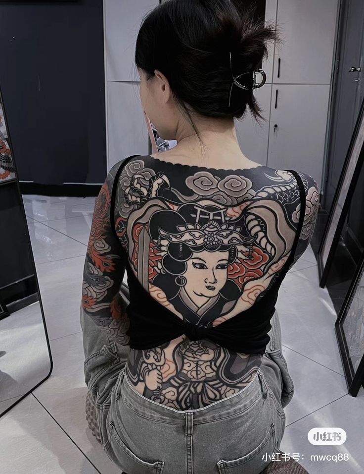 a woman sitting on the floor with tattoos on her back