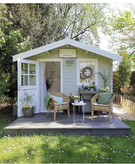 a small white shed with two chairs and a table on the porch in front of it