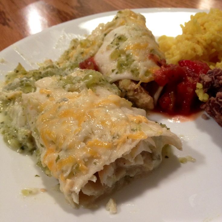 a white plate topped with two enchiladas covered in cheese and sauce next to rice