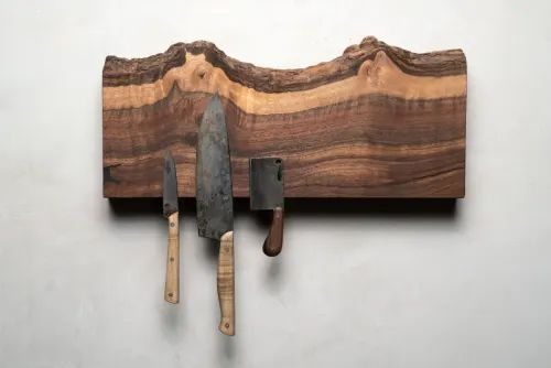 three knives are hanging on a wall with wood and metal blades attached to the knife holder