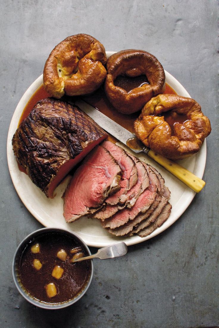 a white plate topped with meat and pastries next to a bowl of dipping sauce