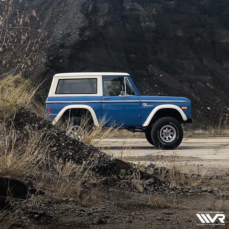 a blue and white truck parked on top of a dirt road next to a mountain