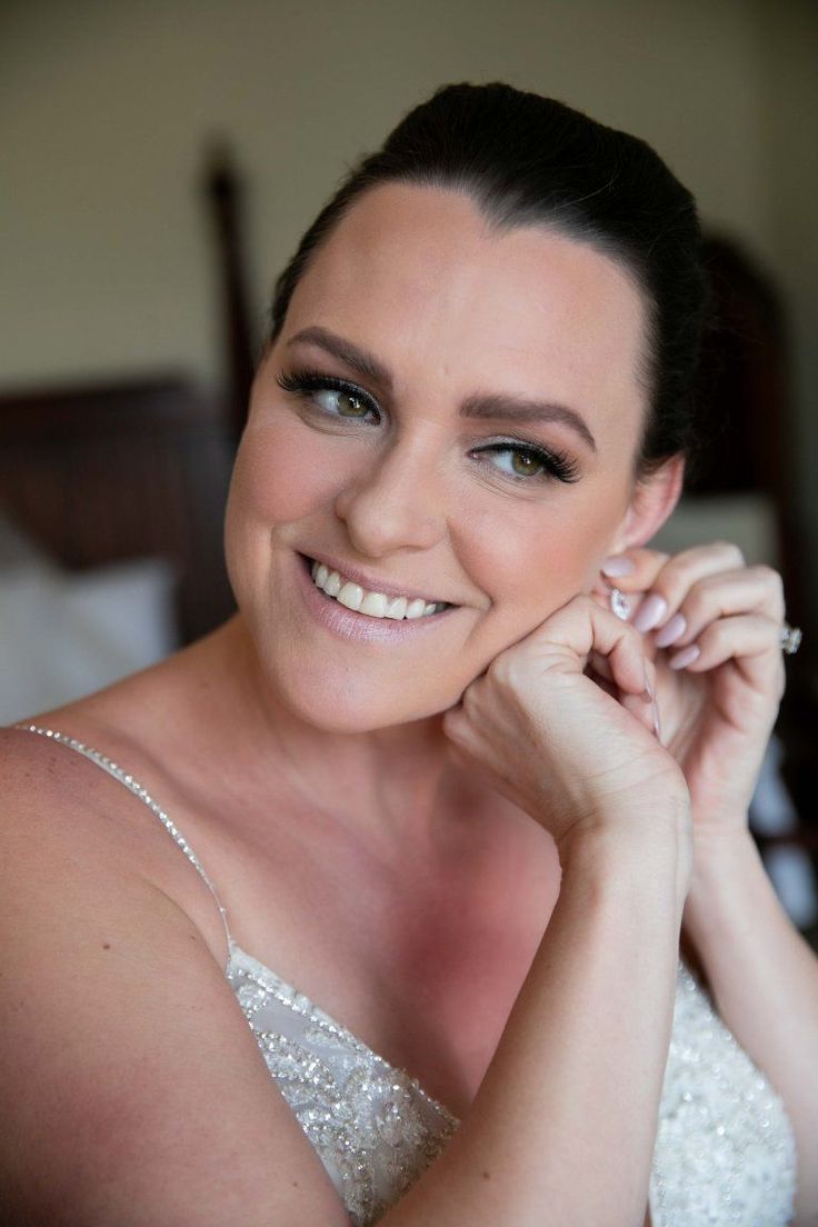 a woman in a wedding dress smiling at the camera with her hand on her cheek