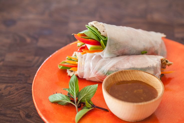 an orange plate topped with two rolls and dipping sauce on top of each other next to a wooden bowl