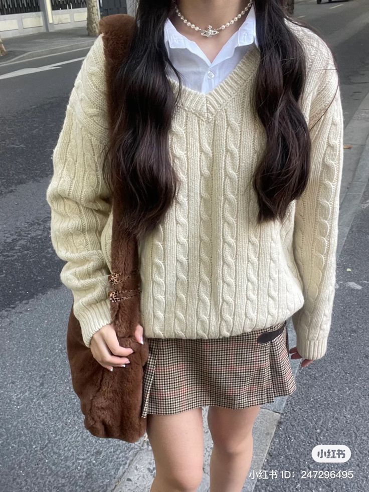 a woman with long dark hair wearing a sweater and skirt