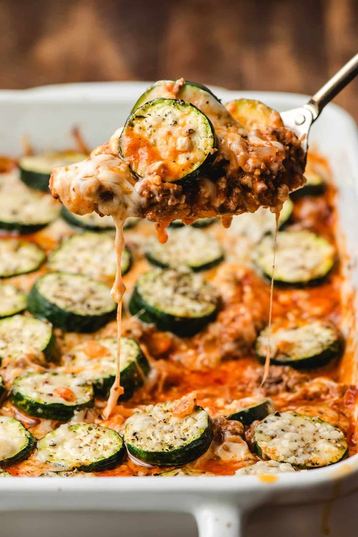 a spoon full of cheese and zucchini casserole being lifted from a baking dish