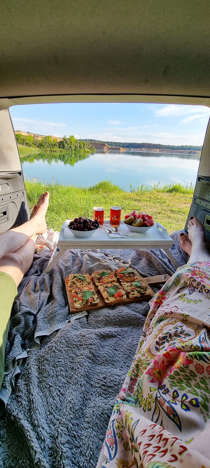 a person laying on a blanket in the back of a car with pizza and drinks