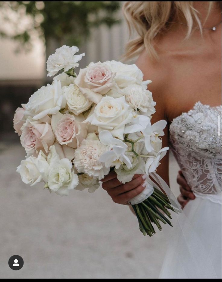 a bride holding a bouquet of white and pink flowers in her hand with the other arm around her waist