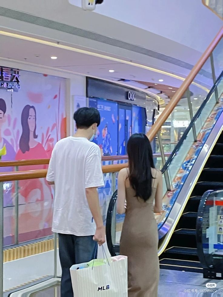 a man and woman walking down an escalator carrying shopping bags