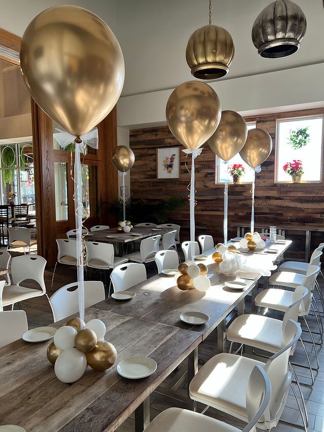 a long table with white chairs and gold balloons