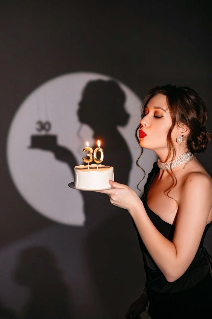 a woman in a black dress holding a cake with candles on it and the shadow of a man behind her