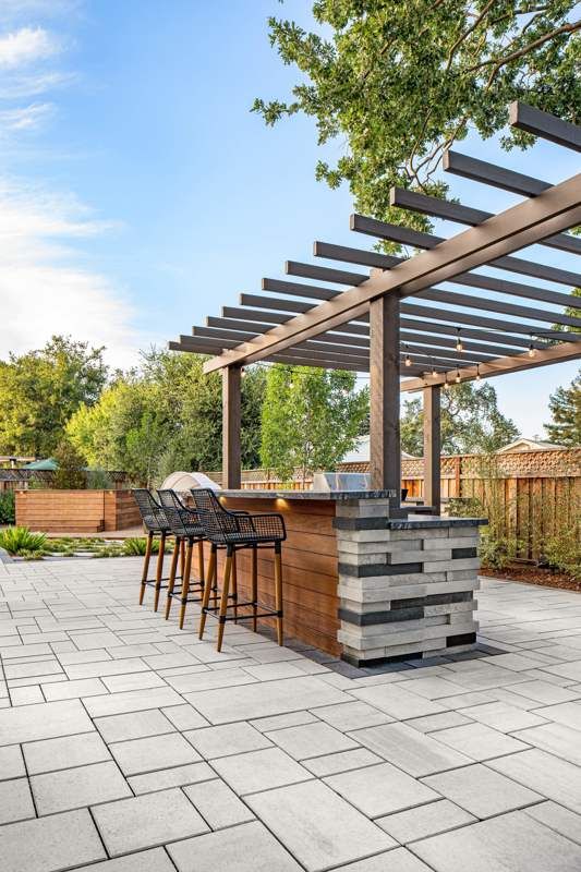 an outdoor bar with stools and tables under a pergolated roof in a backyard