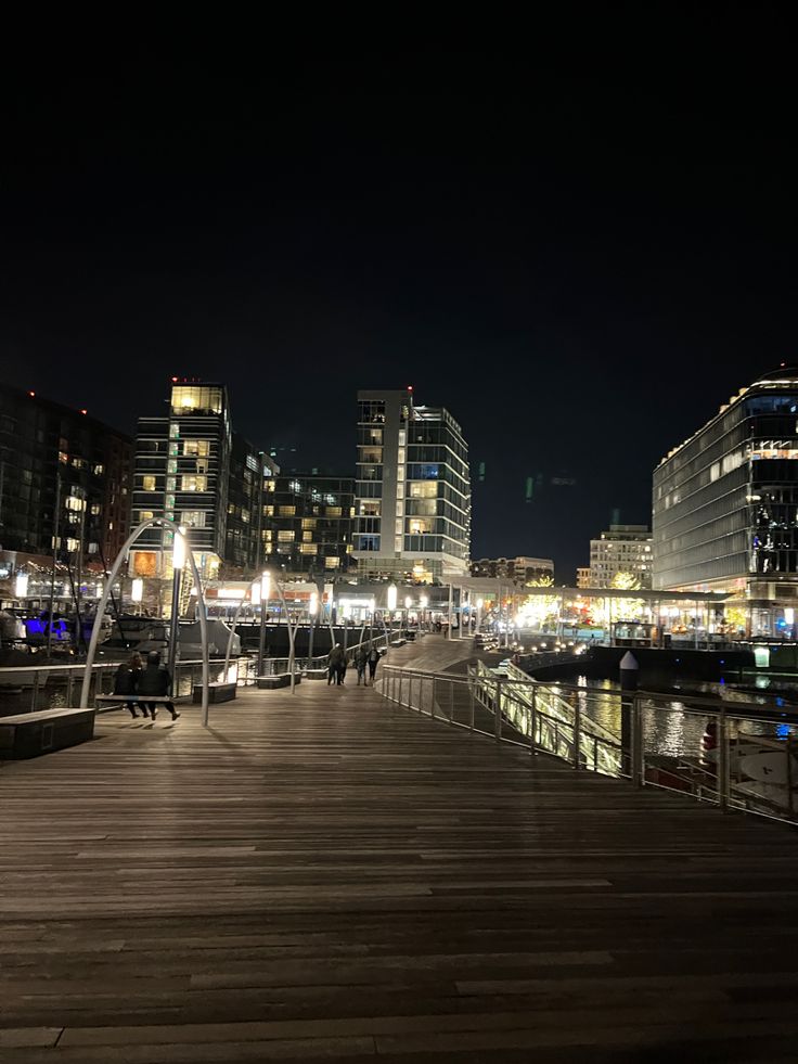 the city is lit up at night with lights on and boats docked in the water