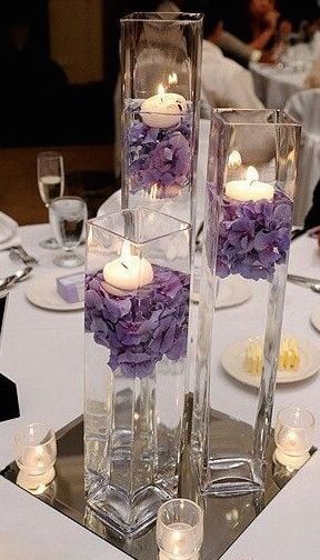 two tall clear vases filled with flowers and lit candles on top of a table