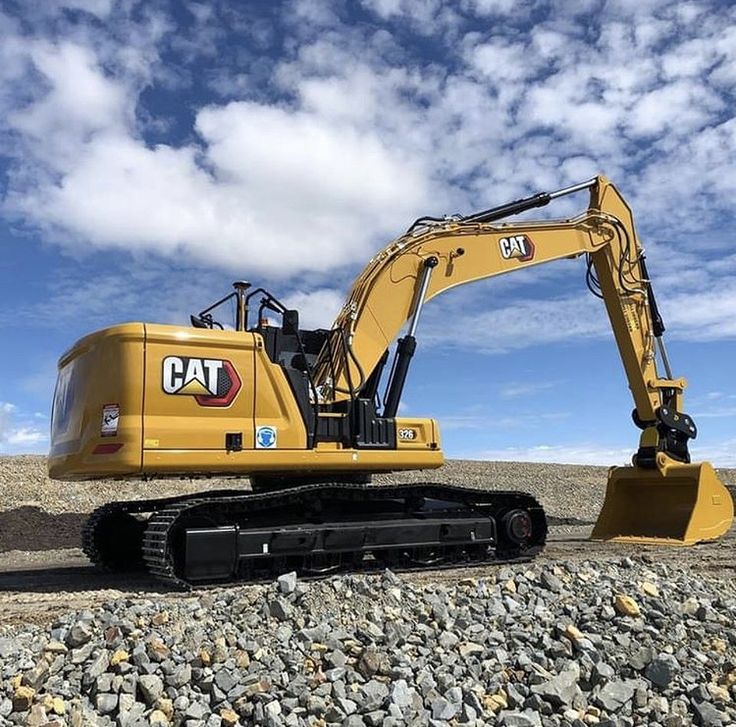 a yellow cat excavator sitting on top of a pile of rocks under a cloudy blue sky