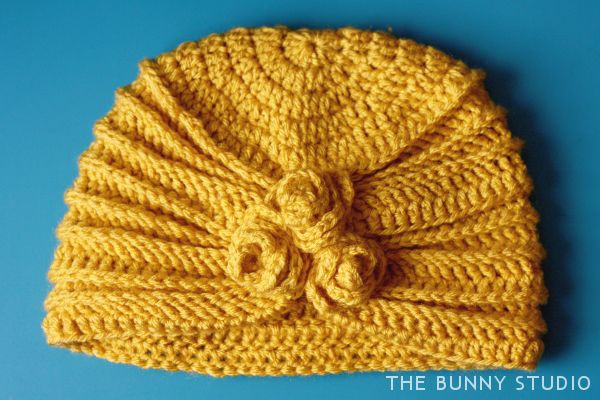 a crocheted yellow hat with a knot on the front and side, sitting on a blue surface