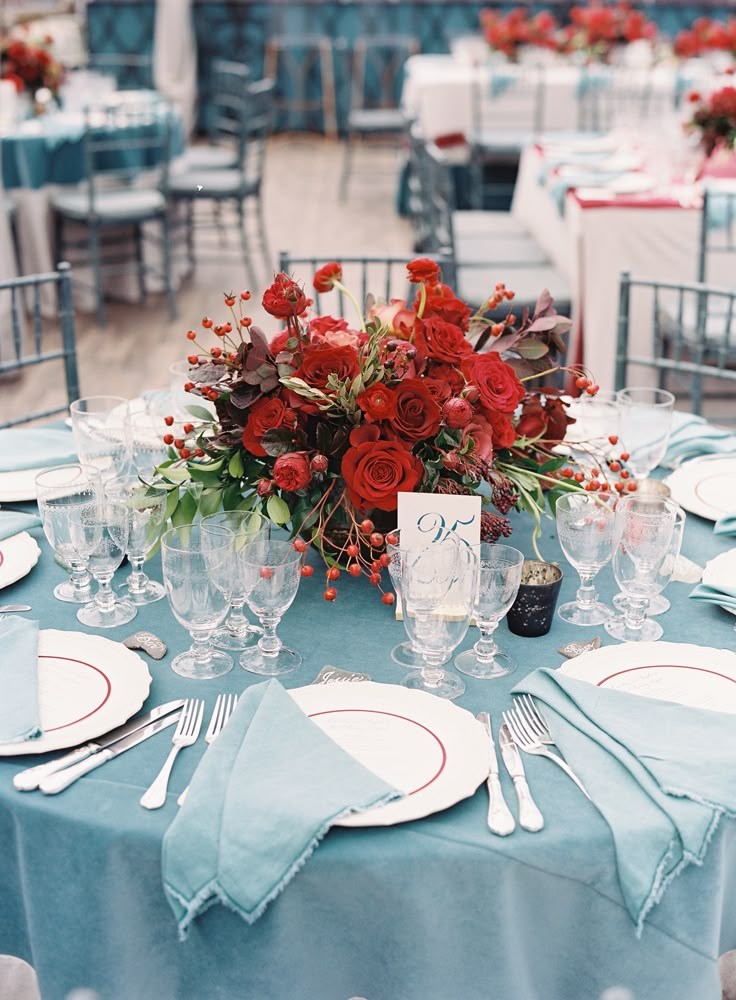 the table is set with red roses and place settings