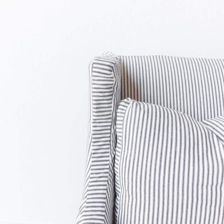 a white and black striped pillow on the back of a chair in front of a white wall