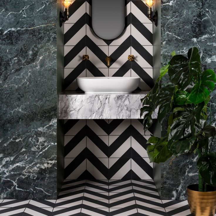 a black and white tiled bathroom with a sink, mirror and potted plant in the corner