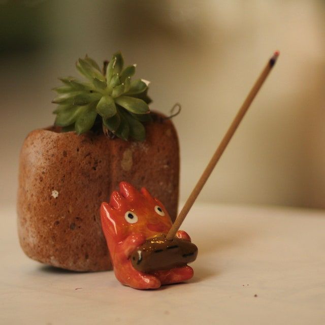 a small toy pig holding a stick next to a potted succulent plant