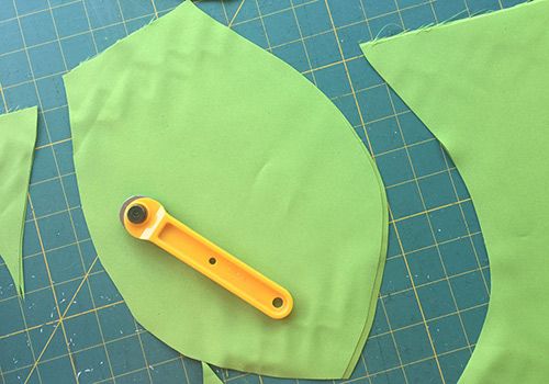 scissors are laying on top of the green paper and cut out leaves with holes in them