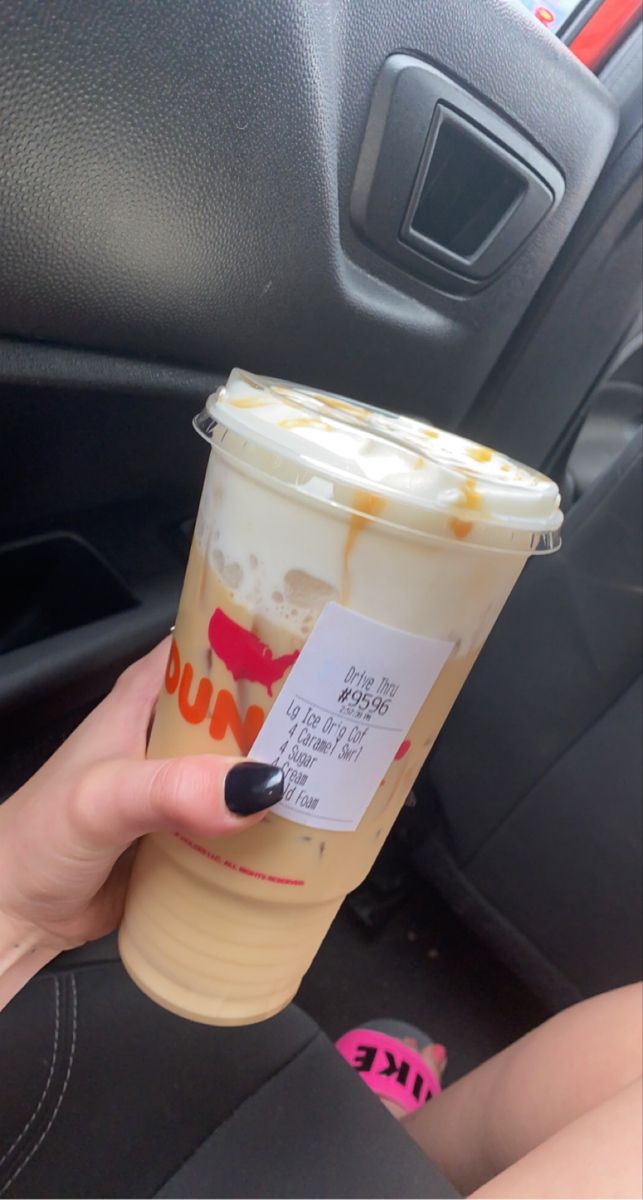 a woman holding up a cup of coffee in her hand while sitting in the driver's seat of a car