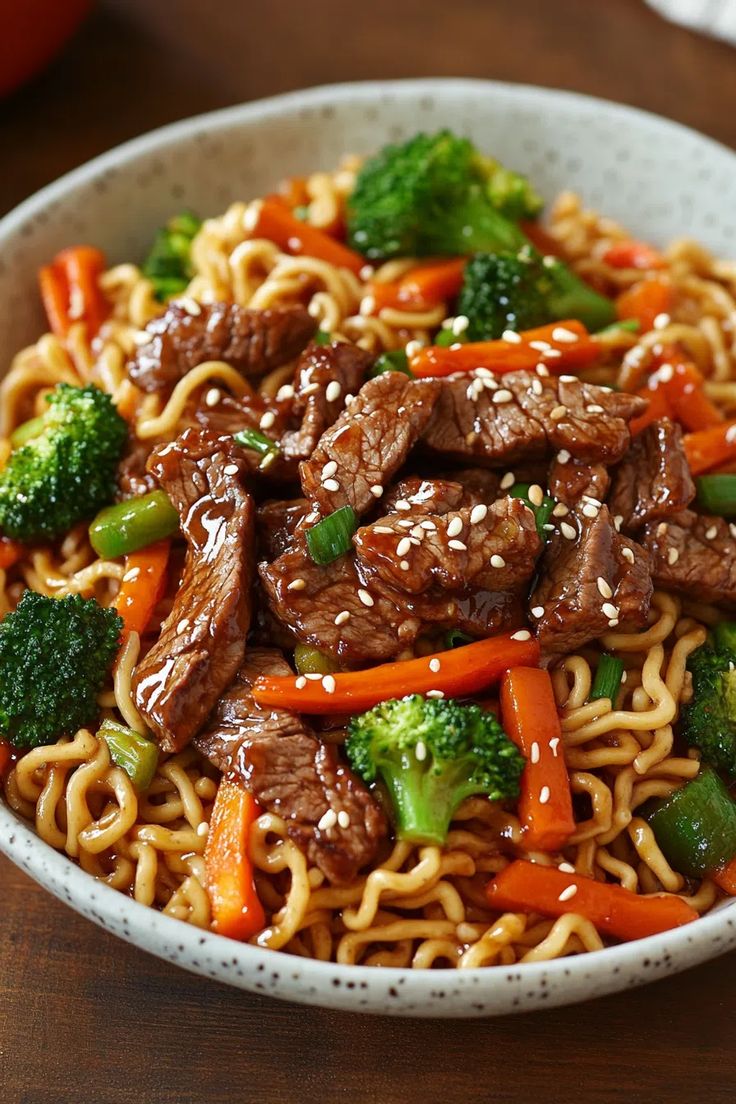 a white bowl filled with beef, broccoli and carrots on top of noodles