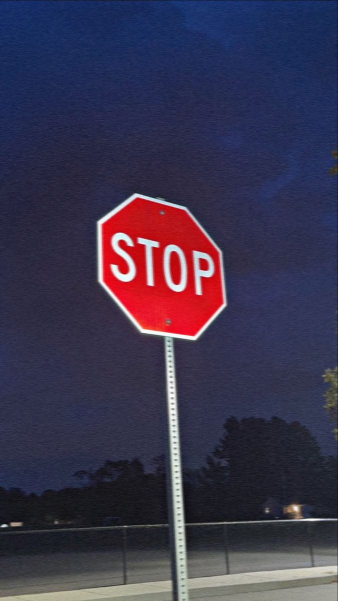 a red stop sign sitting on the side of a road under a dark sky at night