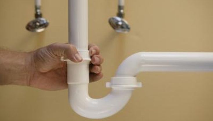 a person holding onto a white pipe in front of some wall mounted faucets