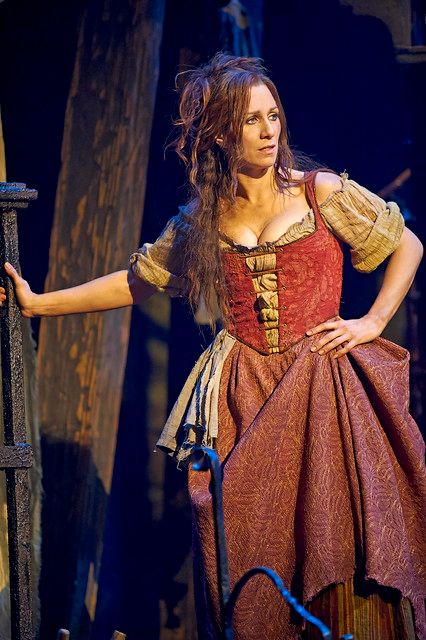 a woman in a red and gold dress standing next to a wooden fence on stage