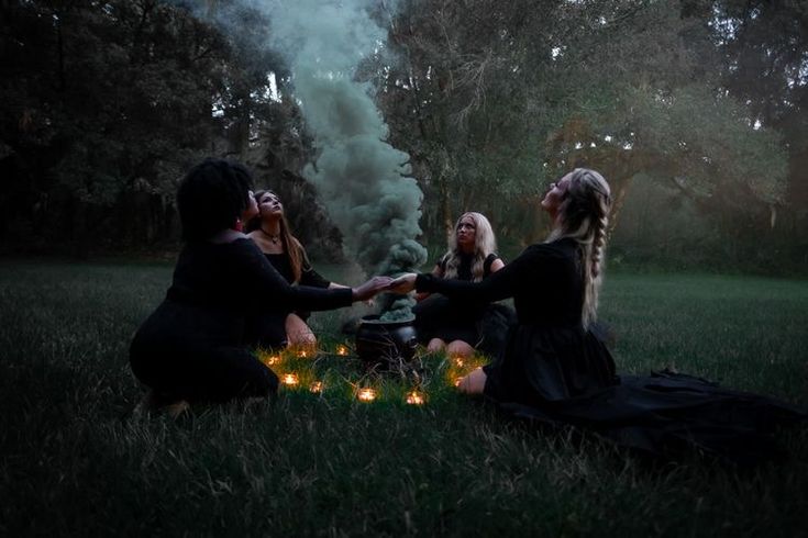 three women sitting in the grass holding candles