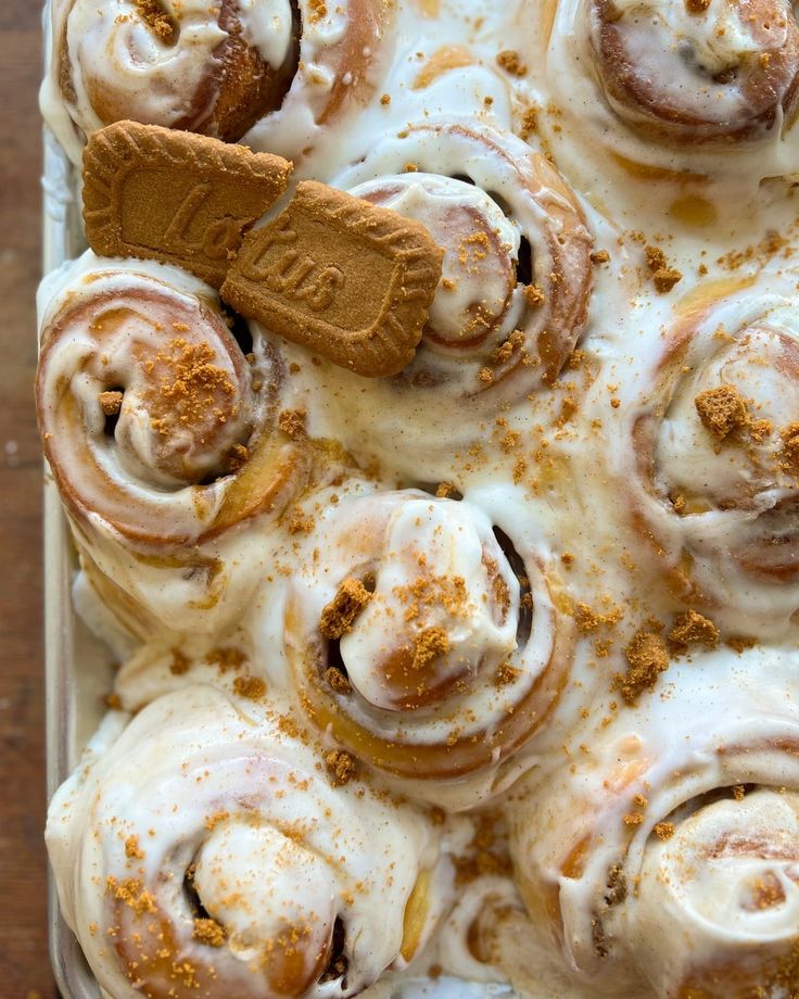 cinnamon rolls in a baking pan topped with icing and cinnamon sticks, on a wooden table