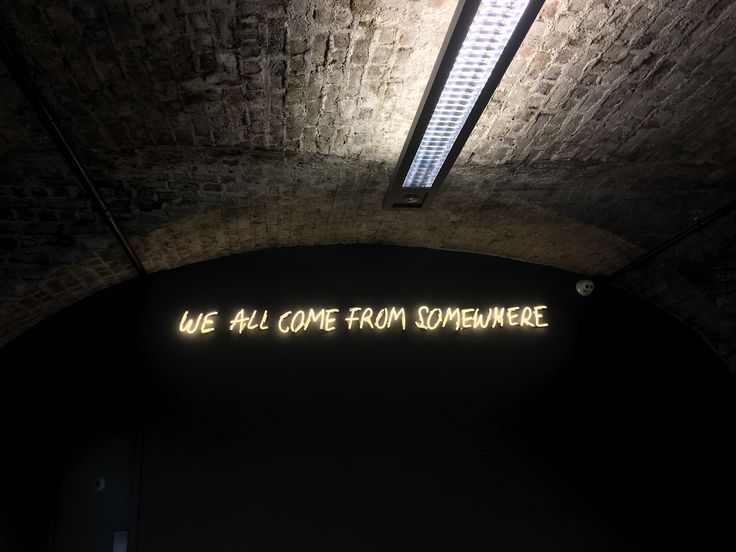 a neon sign that reads we all come from somewhere on the wall in an underground tunnel